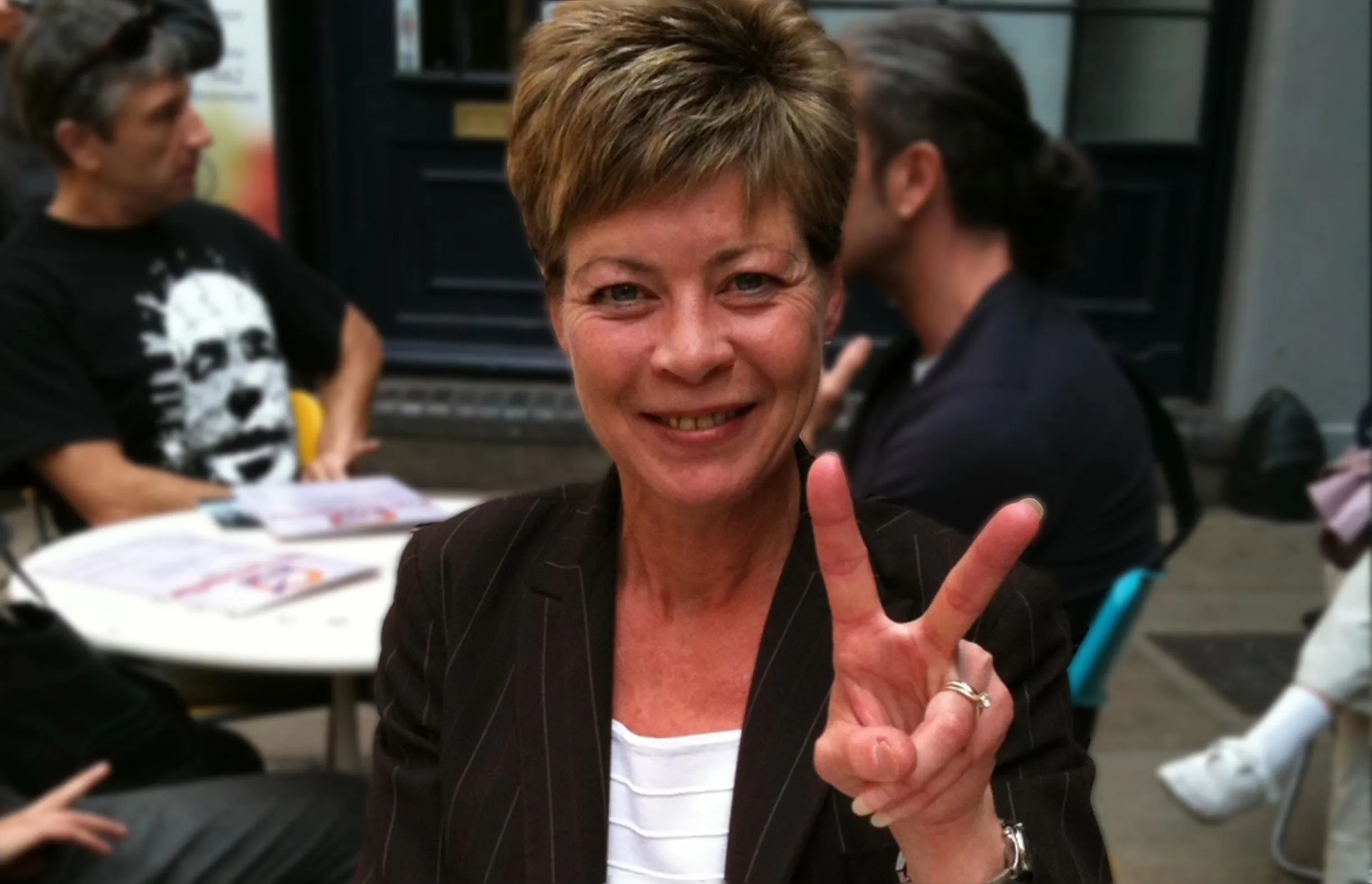 Regina smiles and makes the peace sign while dining outside at a cafe